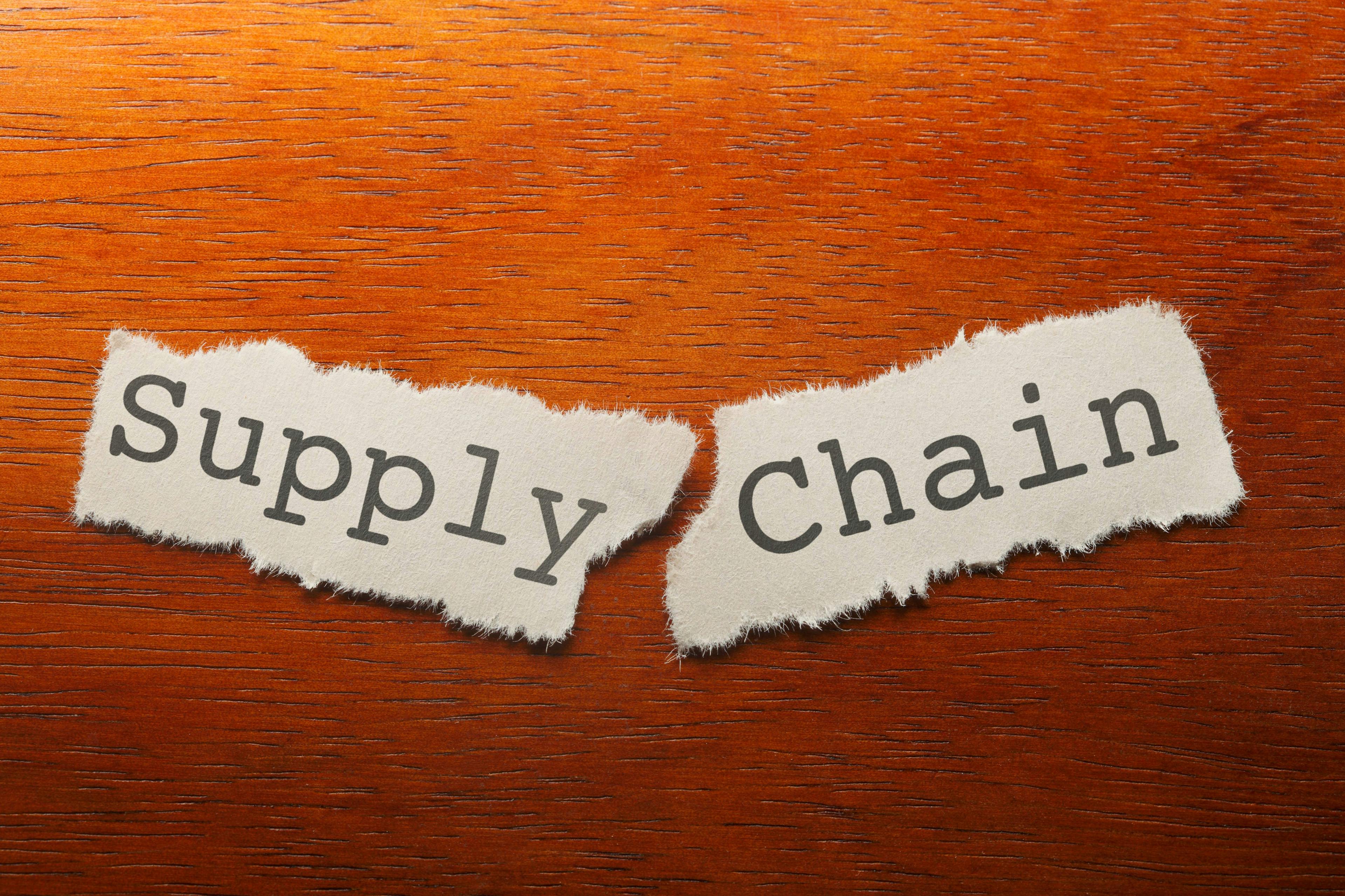 A piece of paper town in half on a desk spelling out “Supply” “Chain”